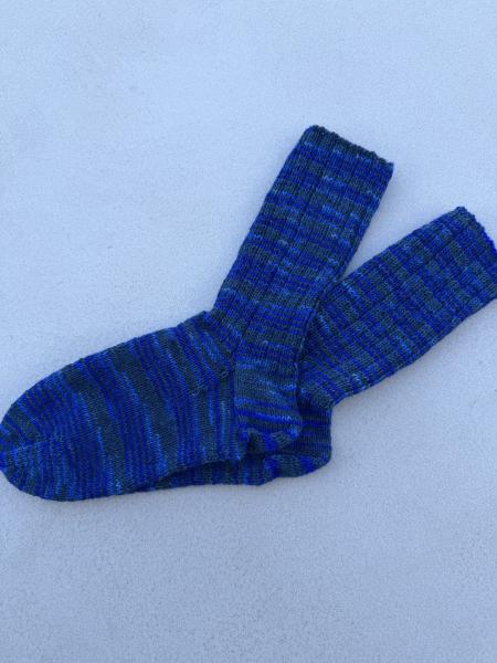 Ein Paar gestrickte Socken aus Herzfasern No. 20 in der Farbe Tiefenblau. Die Socken zeigen ein Ringelmuster aus dunklem Petrolgrau und kräftigem Blau. Klassische Sockenkonstruktion mit Bündchen, Ferse und Spitze.